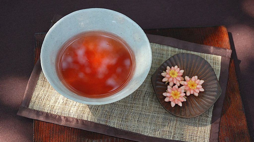 satu gelas teh omija berwarna merah dengan bunga